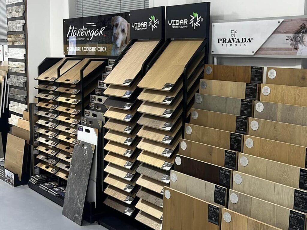 Flooring samples from brands like Vidar, Harbinger, and Pravada on display in a warehouse showroom.